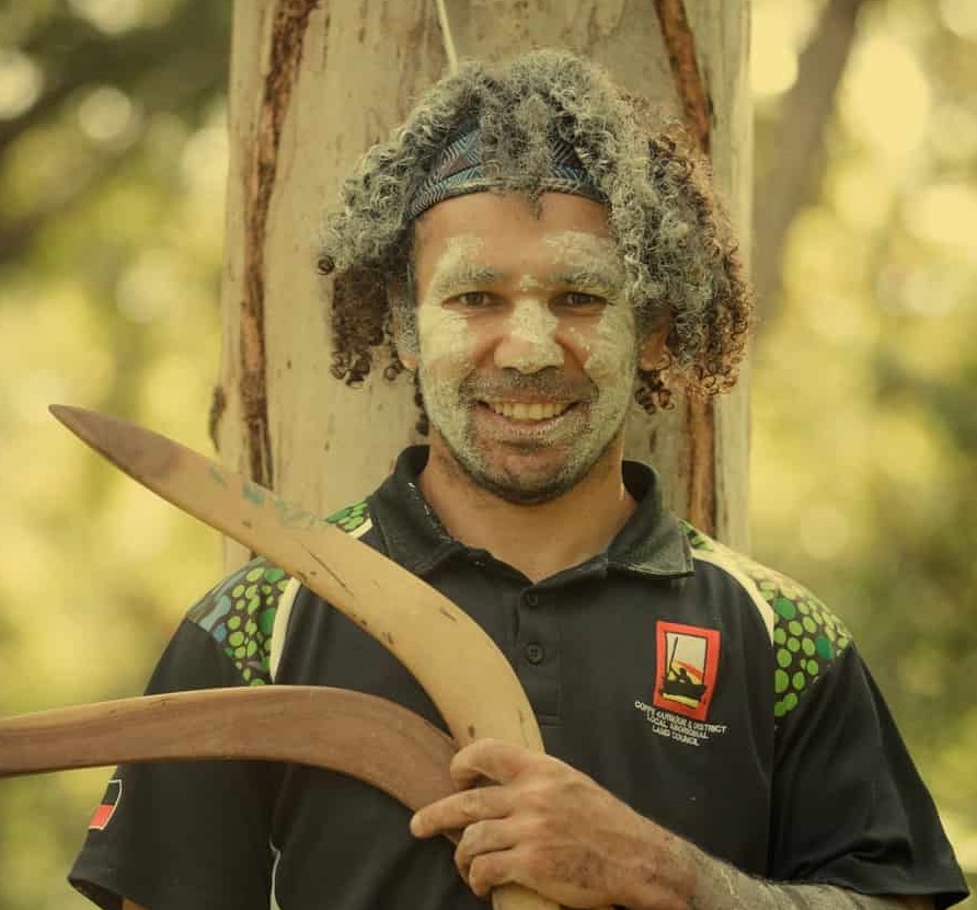 An Aboriginal man in paint with boomerangs