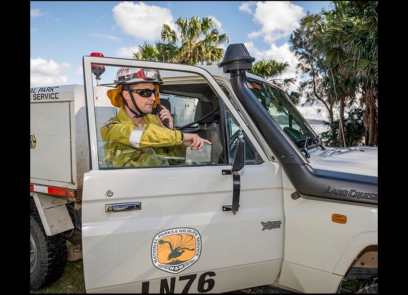 NPWS officr standing with the door of his vehicle open while he talks on the radio. 