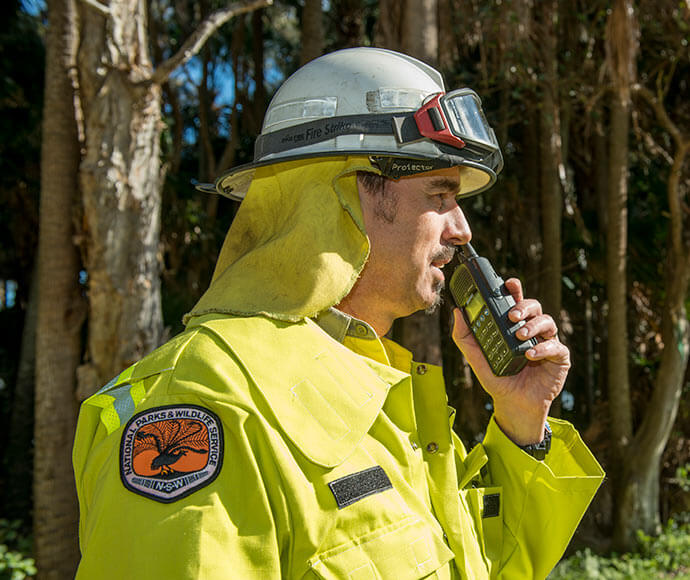 Rural fire fighter wearing protective jacket and helmet, talking on a walkie-talkie.