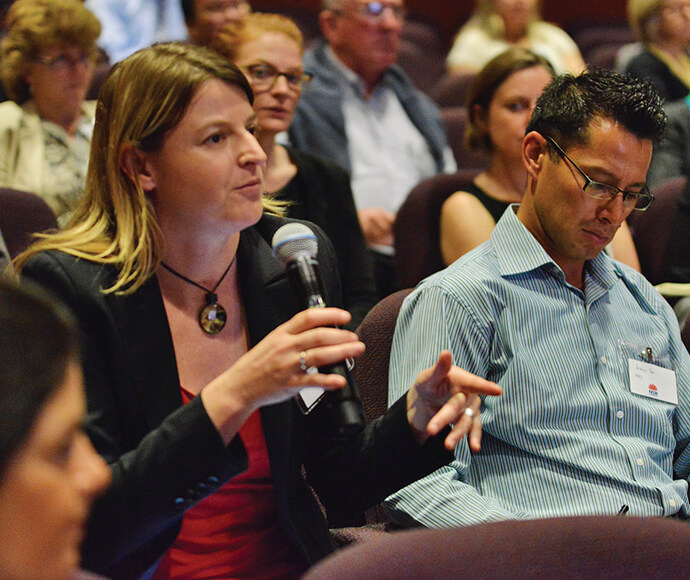 Woman sitting in an audience holding a microphone and asking a question