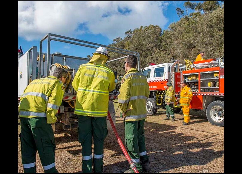 5 volunteer fire fighters standing between 2 fire trucks, inspecting a hose.