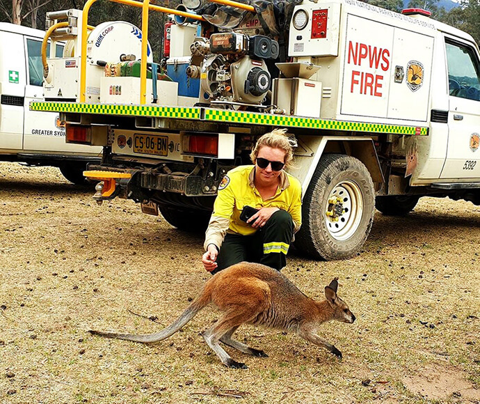 Firefighter helping an injured kangaroo, crouched in front of a firefighting vehicle.