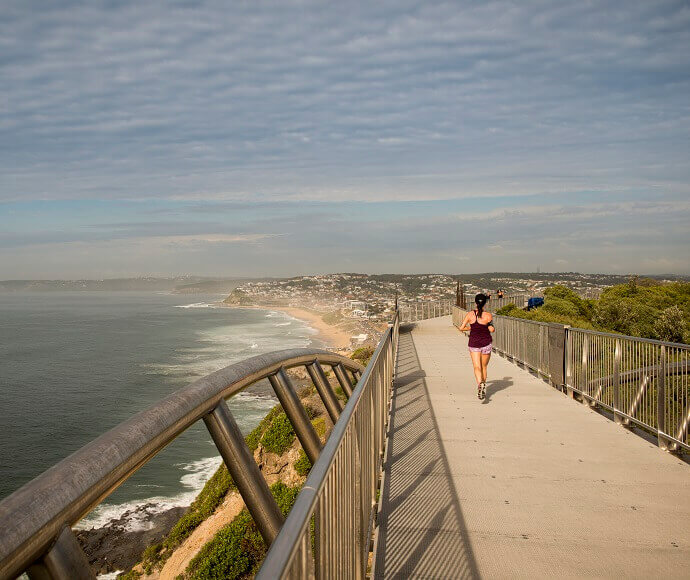 Joggers run along walkway on the headland overlooking the beach at Newcastle