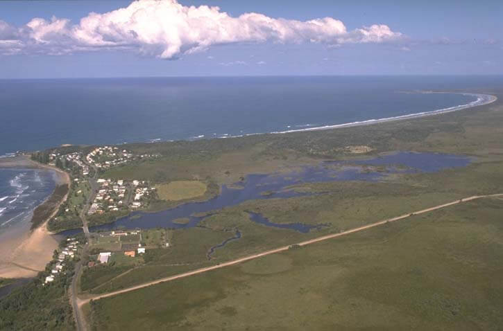 A view of Cakora Lagoon meeting the sea with the coastal village of Brooms Head in the background