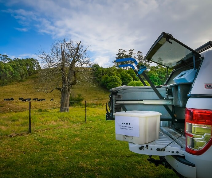 Back of a car in the foreground with sampling equipment on the tailgate. A field with cows is in the bacground