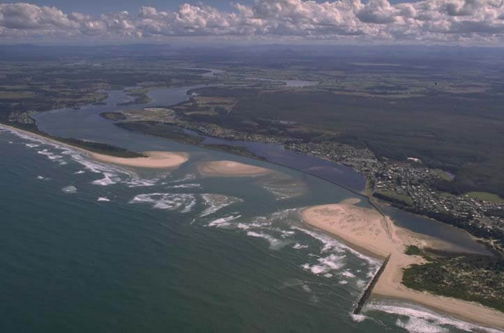 Aerial view of Manning River flowing into the ocean, with visible sandbanks at the river mouth and a nearby town along the waterways.