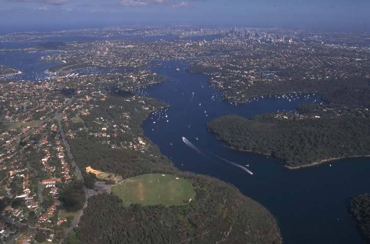 Aerial view of Middle Harbour Creek flowing through dense forests into a turquoise sea with visible sandbanks at its mouth.