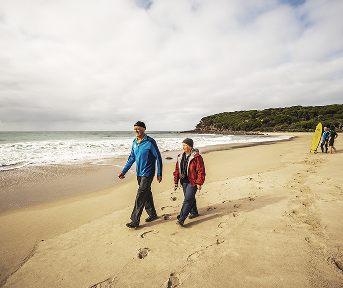 Two people walking the beach, there are another tow in the distance with surf boards. Saltwater campground, Beowa National Park.