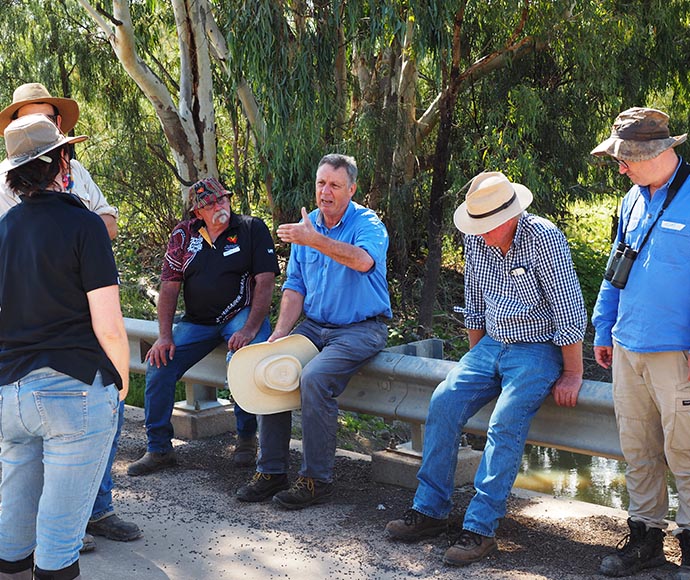 A group of six individuals outdoors, with their faces obscured for privacy, engaged in a discussion or meeting near trees and foliage.