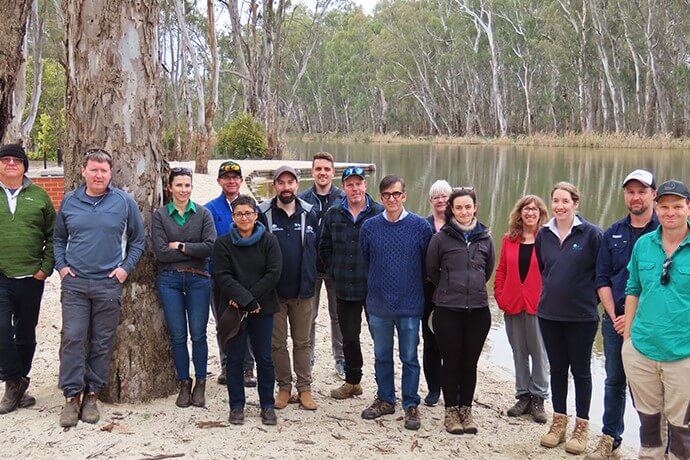 A group of individuals standing in front of a body of water with trees in the background. Their faces are pixelated for privacy.