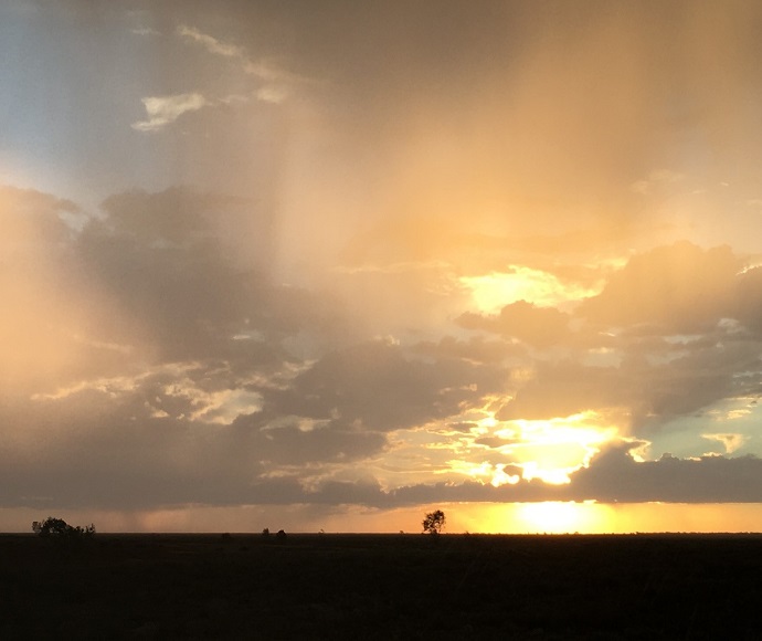 Sunset over an open field with rays of sunlight shining through clouds, creating a gradient from yellow to dark in the sky.