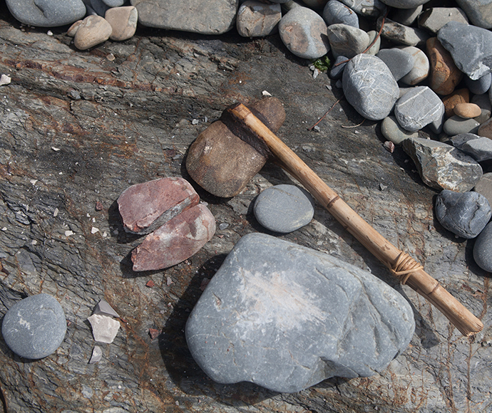 Beautiful Aboriginal artefacts in the foreground, which appear to be a stone axe and tools. The background consists of various small and medium sized rocks and pebbles, as the rocks and tools sit on a coarse rocky surface in Arakwal.