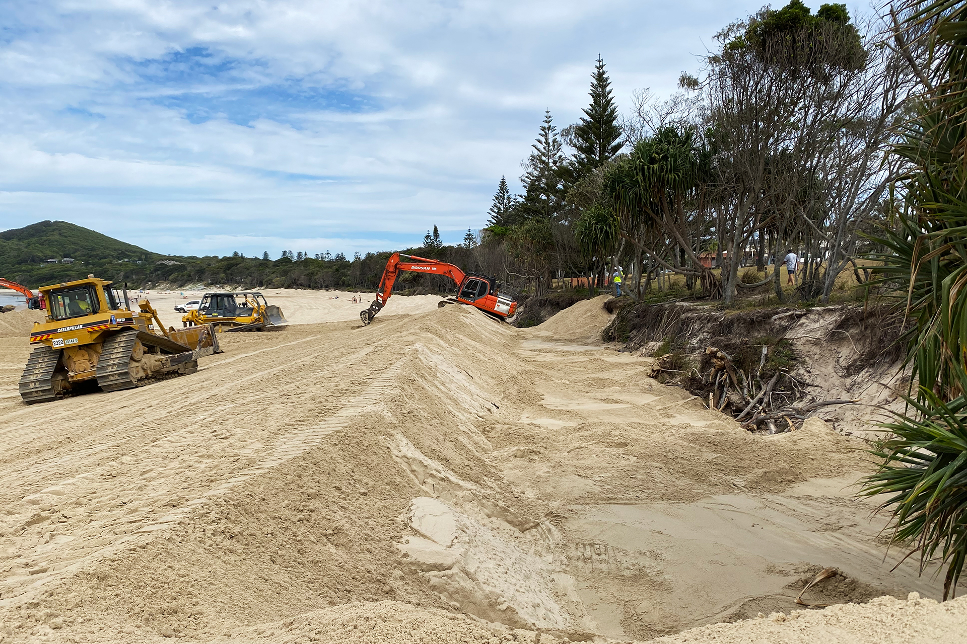 Red and yellow heavy machinery working on a beach, men in hi-vis supervising