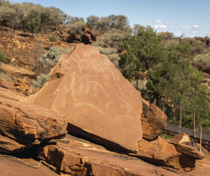 A close-up of ancient Aboriginal rock art at Mutawintji Historic Site, showing pecked engravings on sandstone. The artwork includes handprints, animal tracks, and circular motifs etched with fine detail. The reddish-brown sandstone enhances the visibility of these culturally significant symbols, representing stories of heritage, spirituality, and connection to Country. This preserved site provides insight into Aboriginal history and traditions, highlighting the importance of cultural continuity.