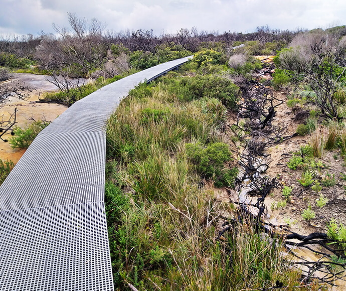 A sturdy raised metal track next to an eroded strip of clay with sticks strewn across it.