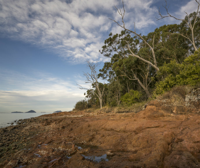 A panoramic view of Soldiers Point, an area declared as an Aboriginal Place, featuring a serene coastal landscape with lush greenery and calm waters under a clear sky.