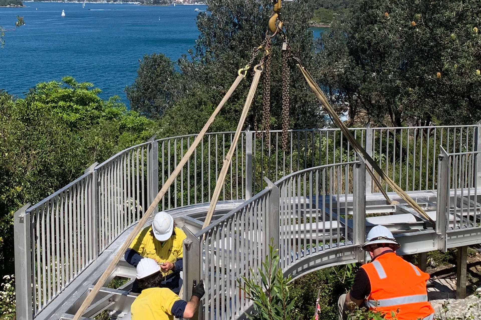 Men assisting the crane installation of a new pedestrian bridge.