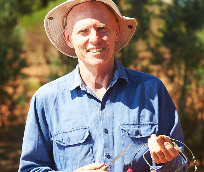 Dr David Eldridge wears a straw hat and holds research tools in his hands