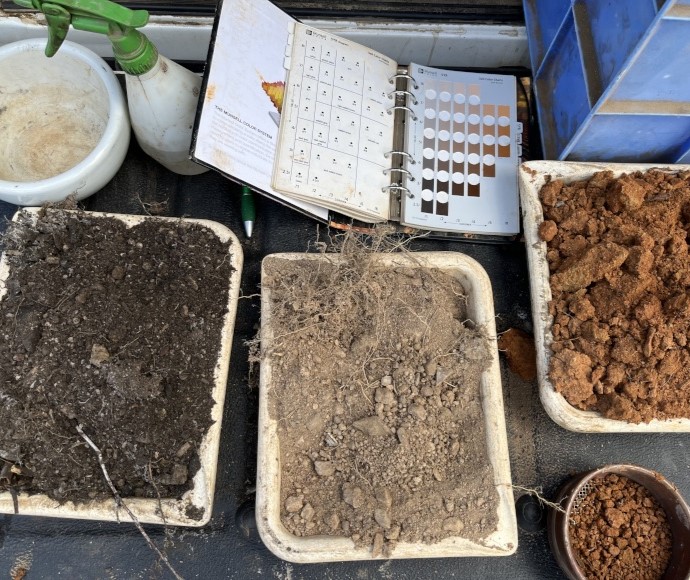 three trays of soil in distinctly different colours. One is dark brown, another light sandy and the other is red.