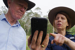 A woman holding up her phone showing a man how to use it