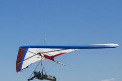 Person in a red and blue hang-glider in the sky. 