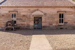 Single-story stone building with a shingled roof, central door, two windows, and old equipment on the left side